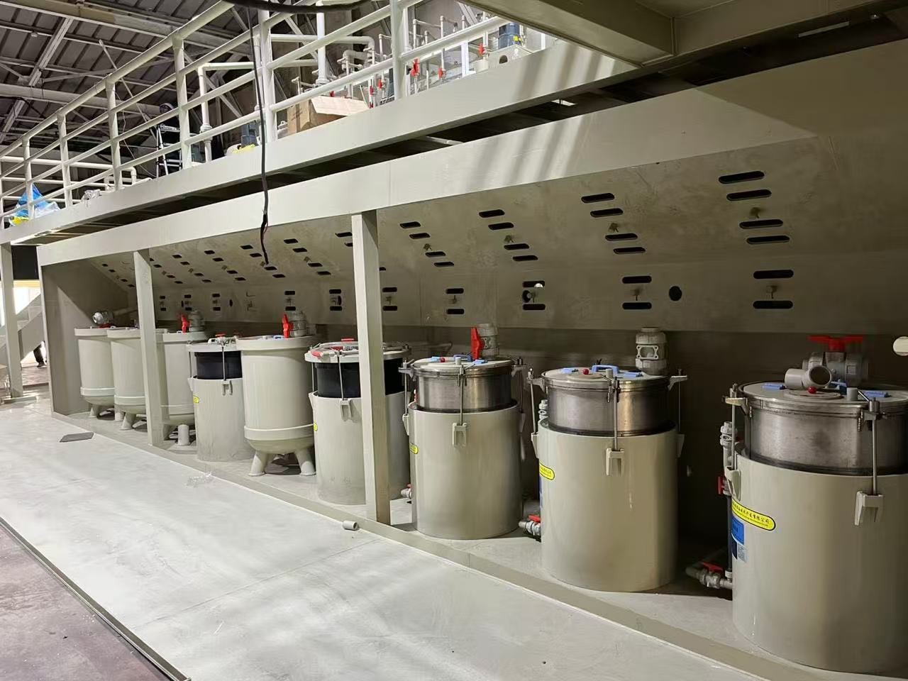 工場内に並ぶ複数の産業用処理タンクと攪拌装置の列。上部には点検用の通路が設置されています。