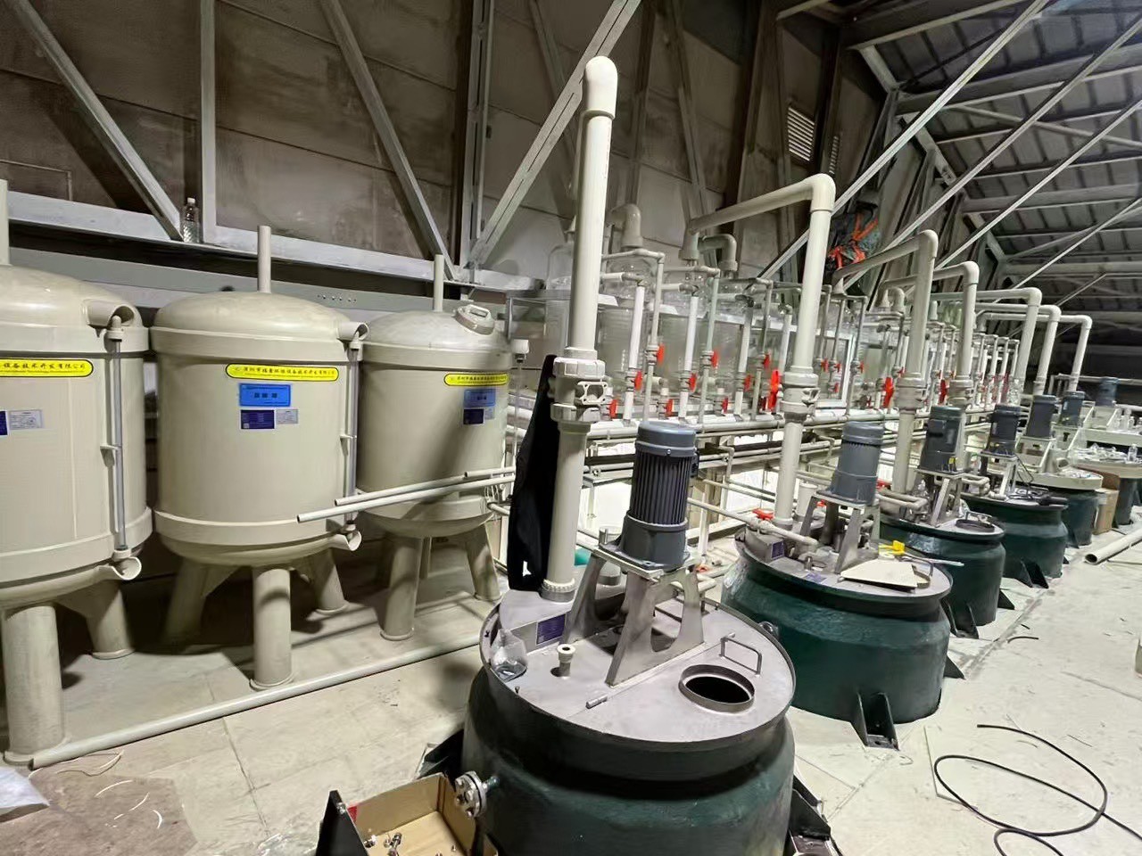 工場内に並ぶ産業用の大型濾過タンクとモーター付きの処理槽、複雑な配管システムの様子。