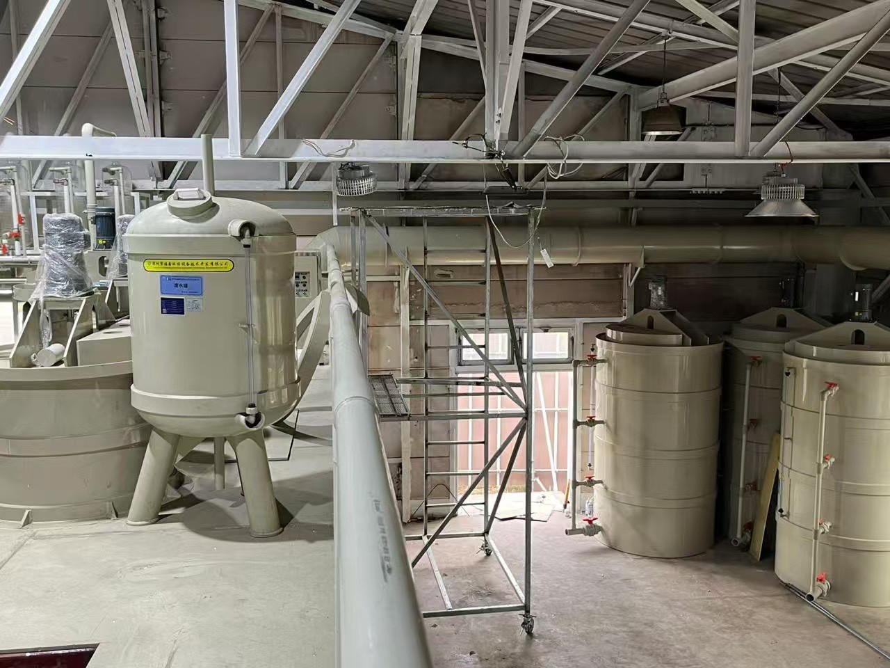 大型のタンクや配管、金属製の足場が設置された、化学プラントまたは水処理施設のような工場の内部。